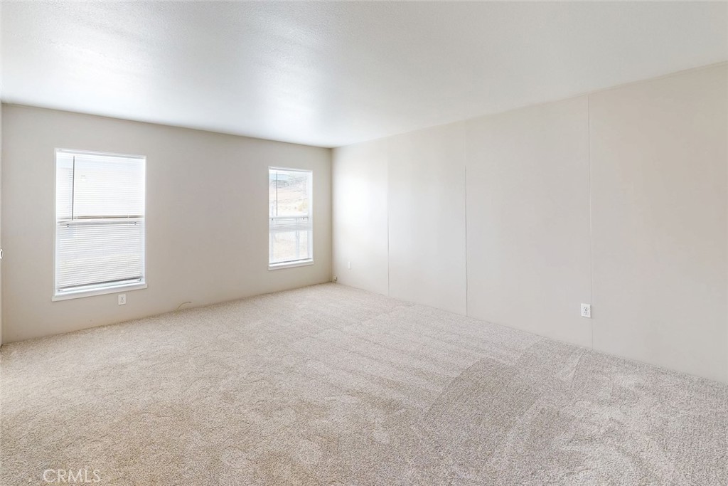 Empty carpeted room with two windows and blinds.