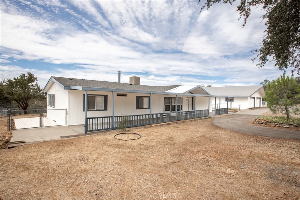Single-story home with a long covered porch, dark railing, and dry dirt yard.