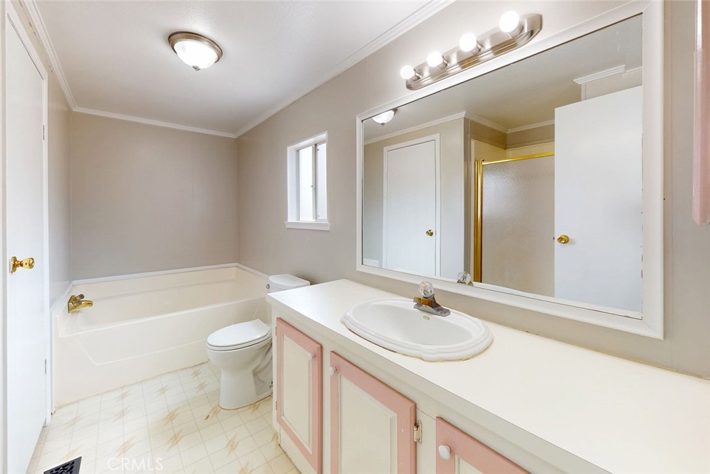 Bathroom with built-in tub, long pink-trimmed vanity, oval sink, and large mirror.