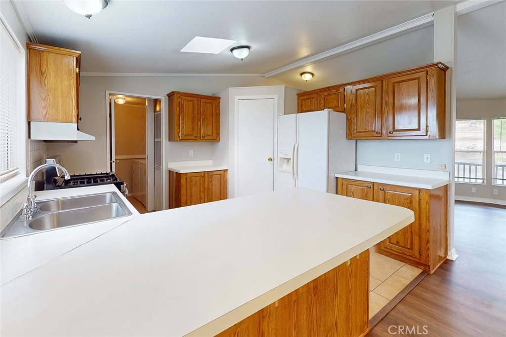 Kitchen with wood cabinets, a large white peninsula, double sink, and gas cooktop.