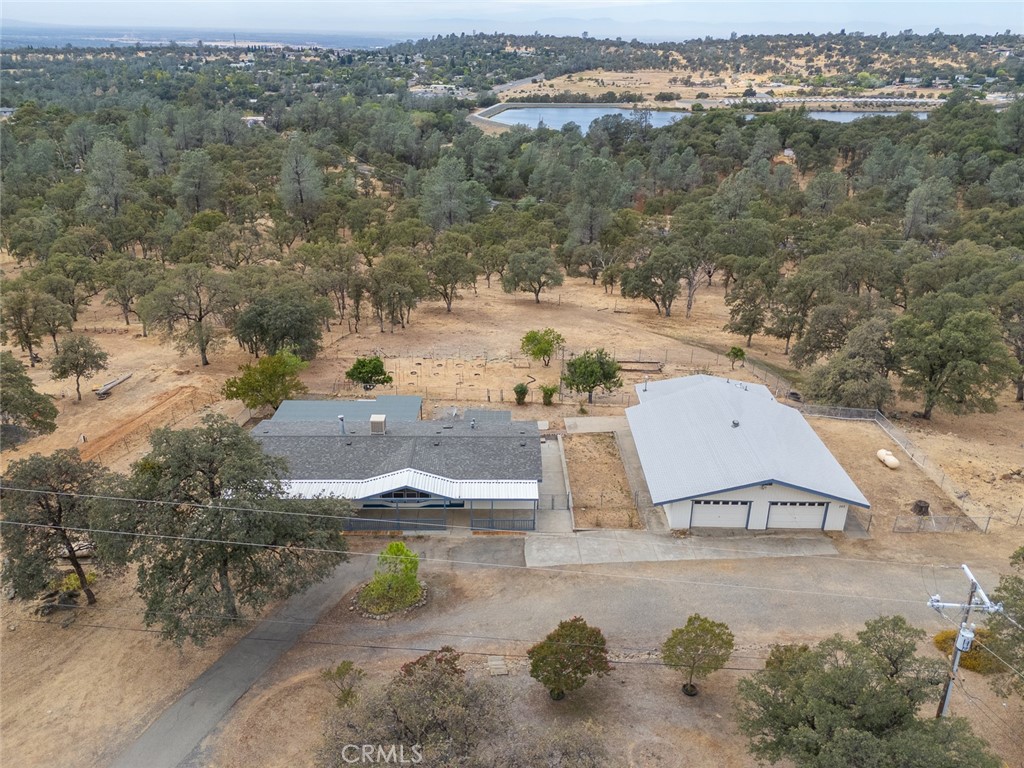 Rural home and large detached garage amid dry, oak-dotted acreage, with a reservoir in the distance.