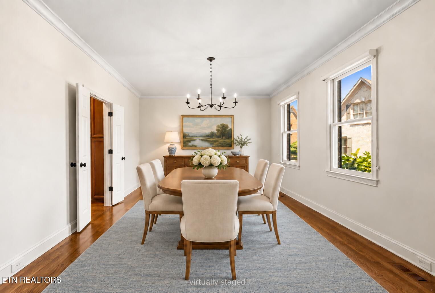 Dining room with an oval wood table, cream chairs, chandelier, and pale blue rug.