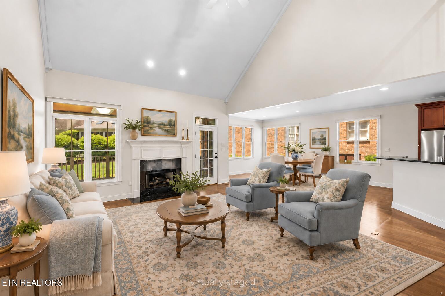 Living room with a vaulted ceiling, white fireplace, large windows, and open dining area.