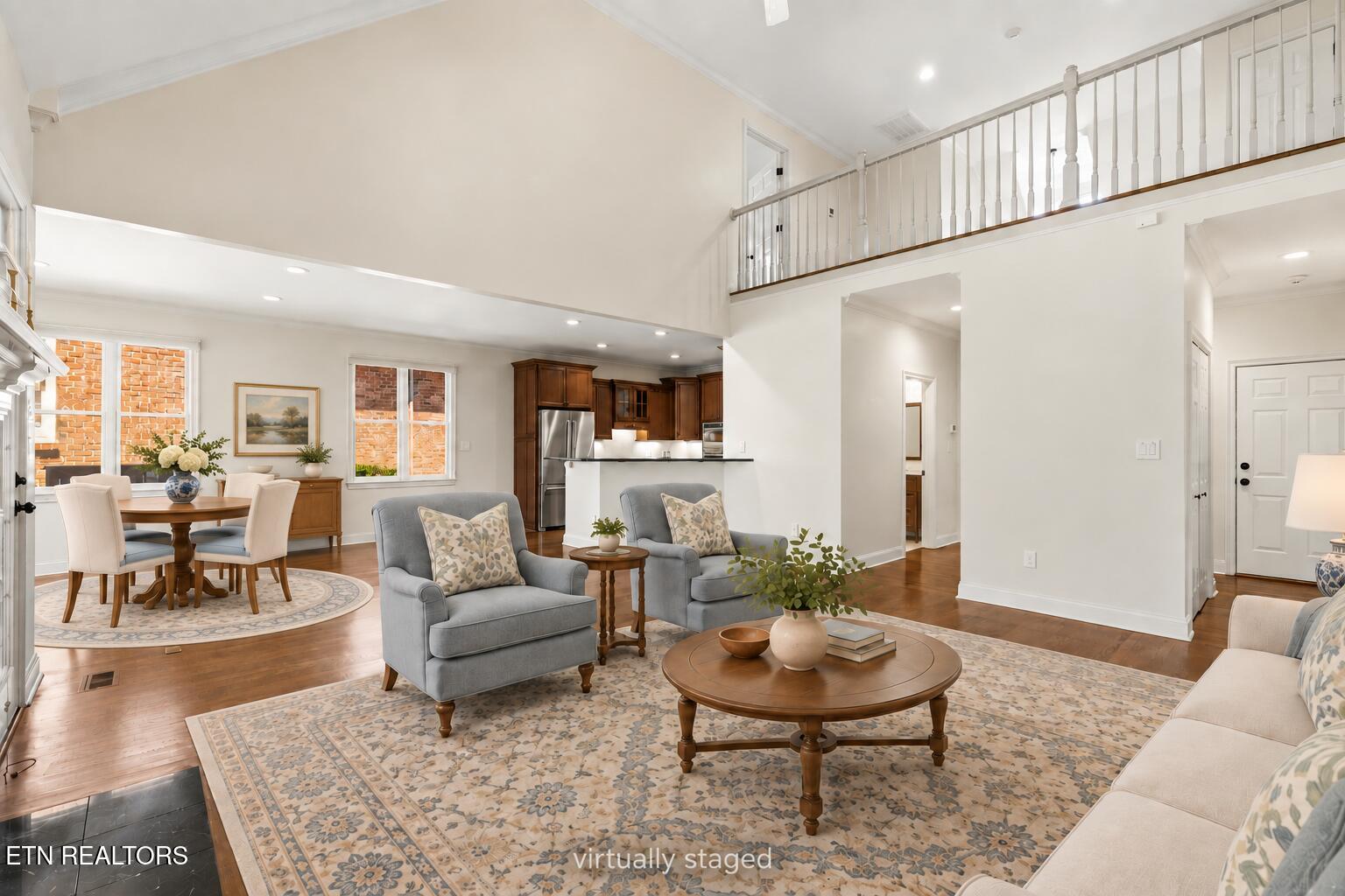 Double-height living room with gray seating and patterned rug, open to the dining area and kitchen.