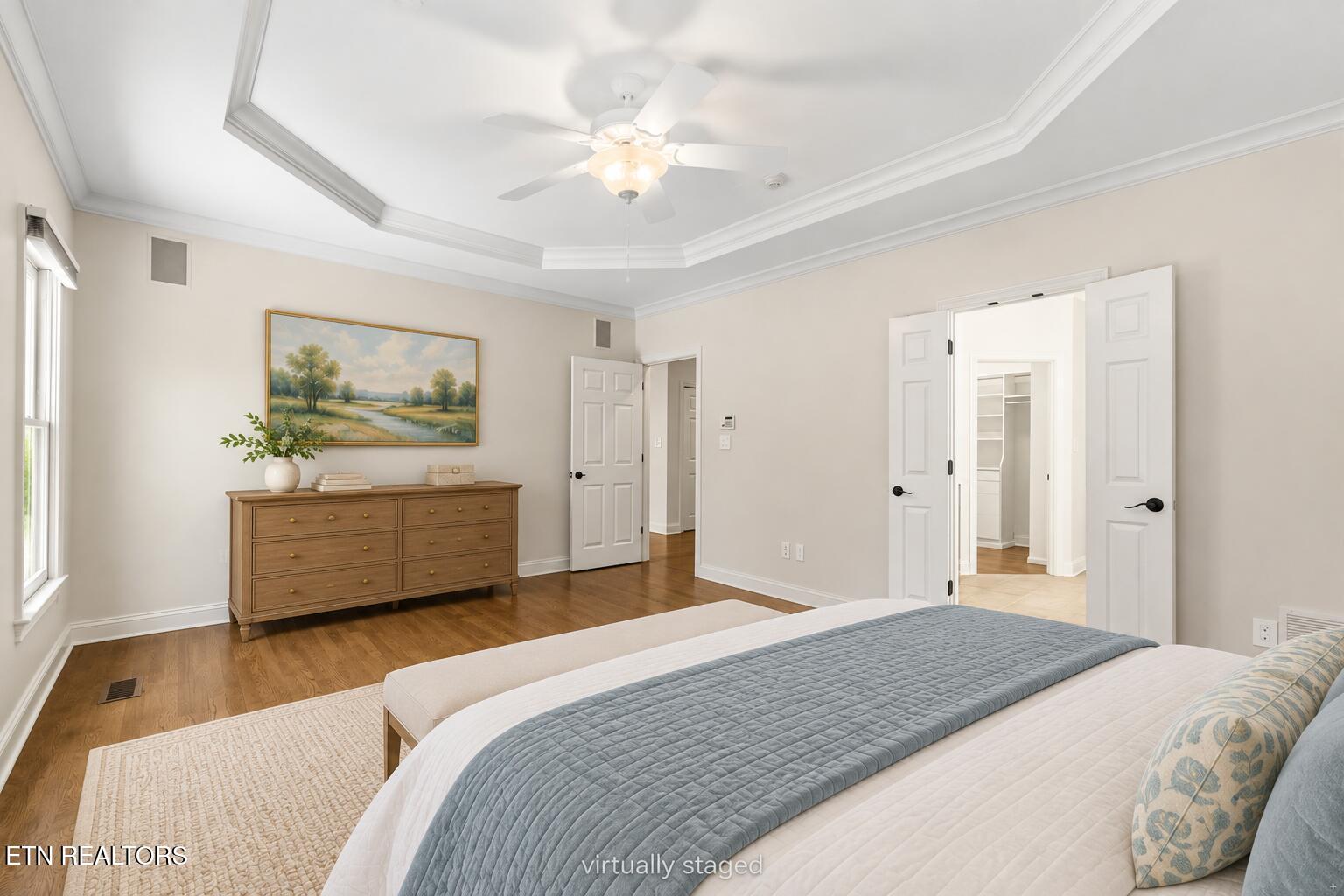Bedroom with a tray ceiling, hardwood floors, and open doors to a walk-in closet.