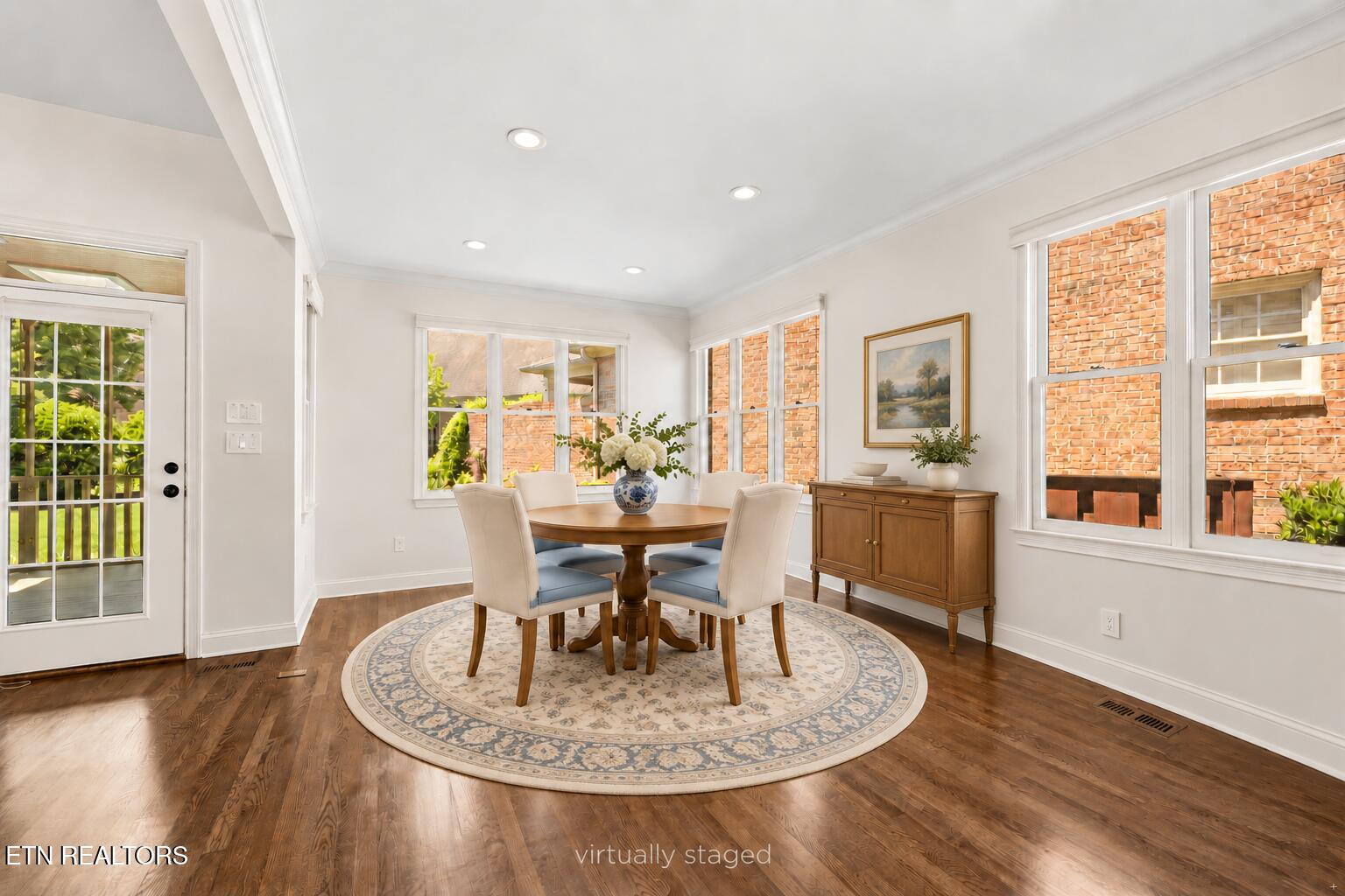 Virtually staged dining room with a round table, upholstered chairs, patterned rug, and large windows.