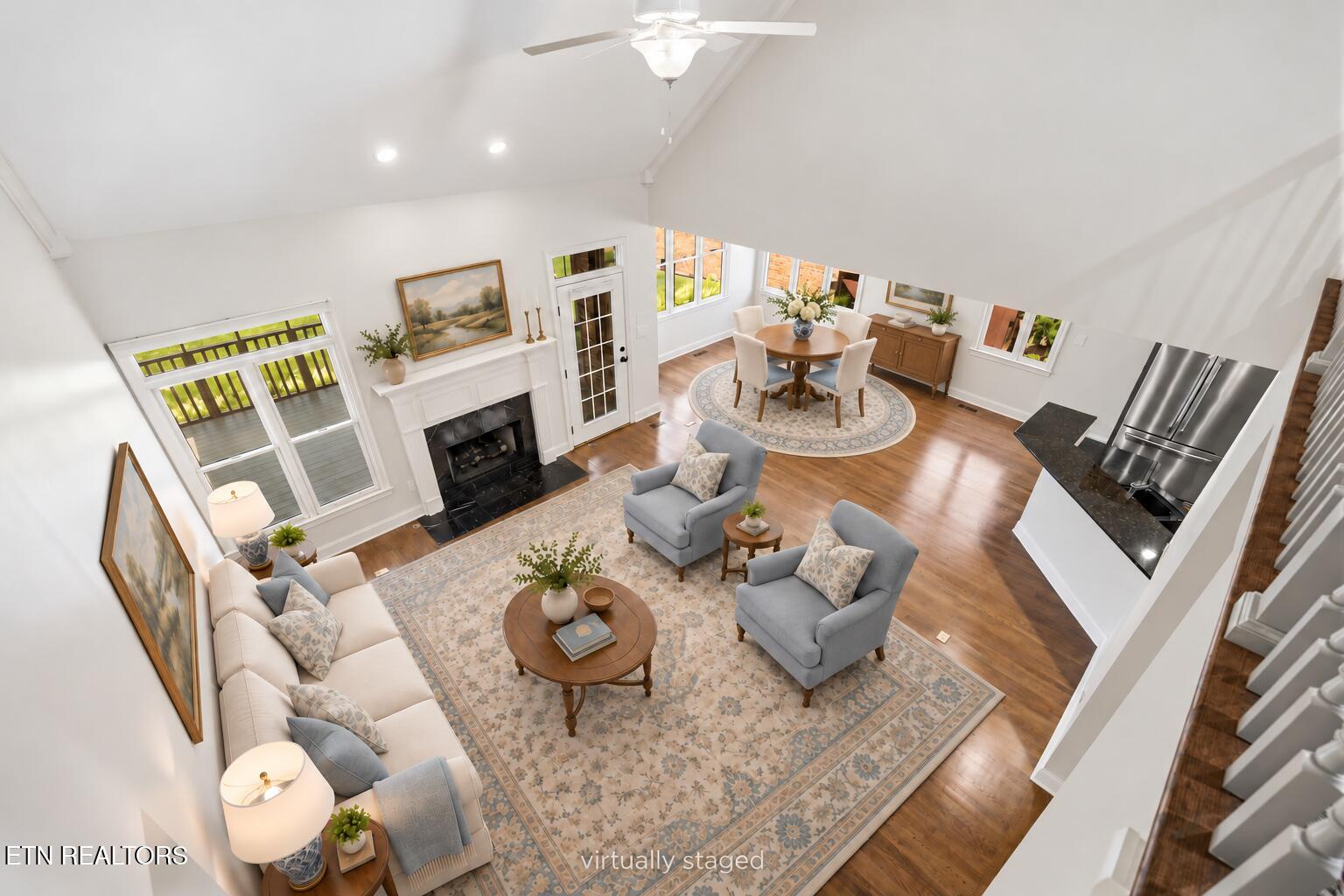Living room with vaulted ceiling, white fireplace, hardwood floors, and seating beside an adjoining dining area.