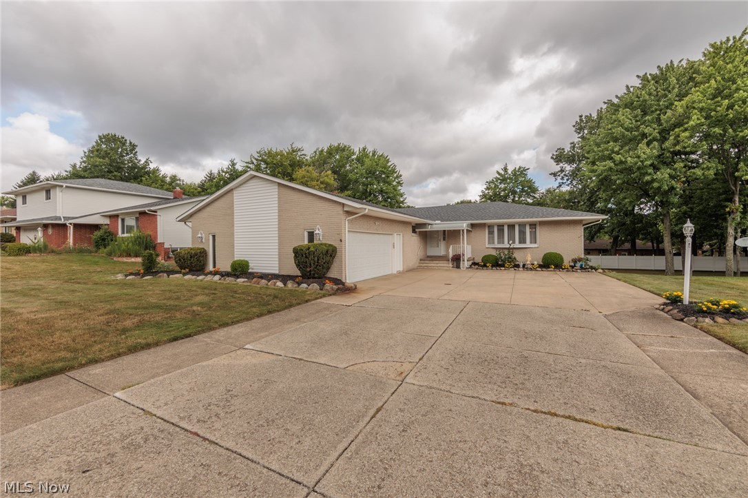 Single-story beige home with brick accents, attached garage, and broad concrete driveway.