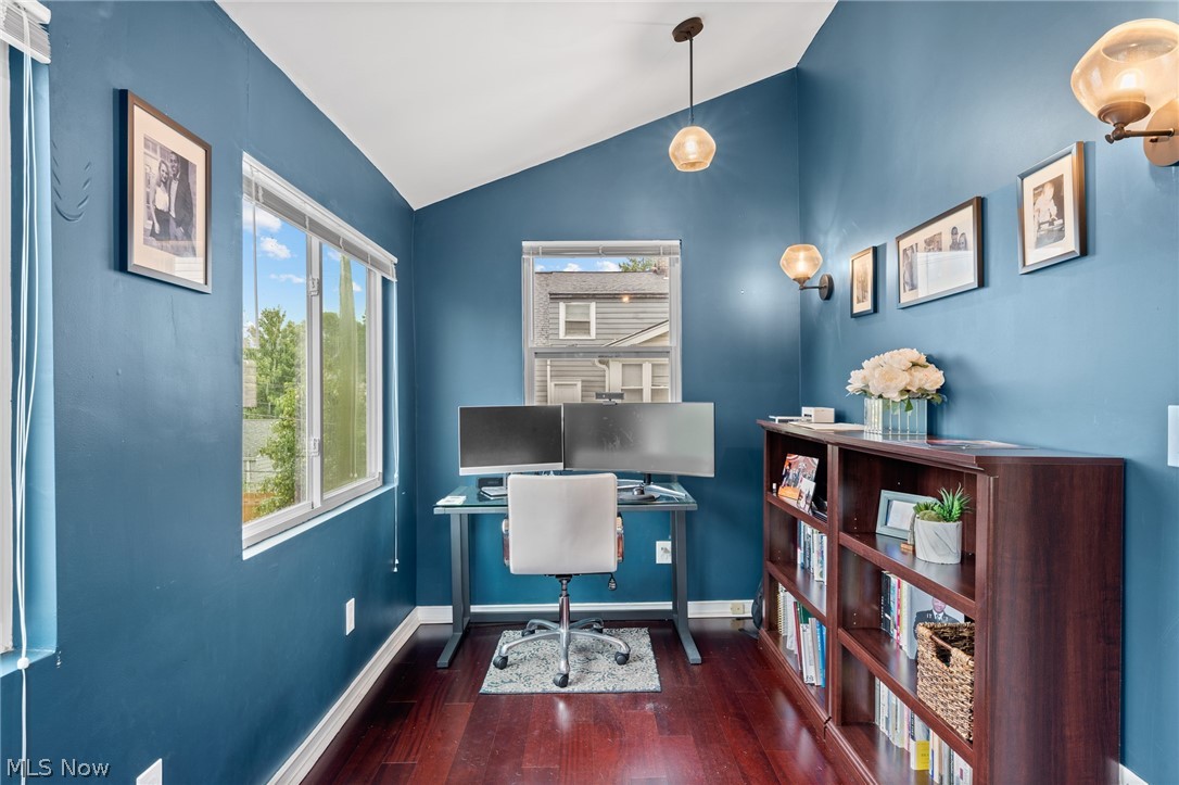 Blue home office with a dual-monitor desk, white chair, hardwood floors, and a dark wood bookcase.
