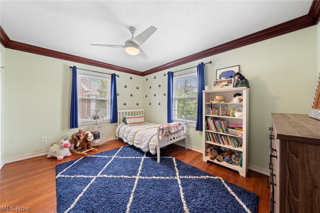 Bedroom with a white bed, blue curtains, a toy-filled bookcase, and a navy grid-pattern rug.