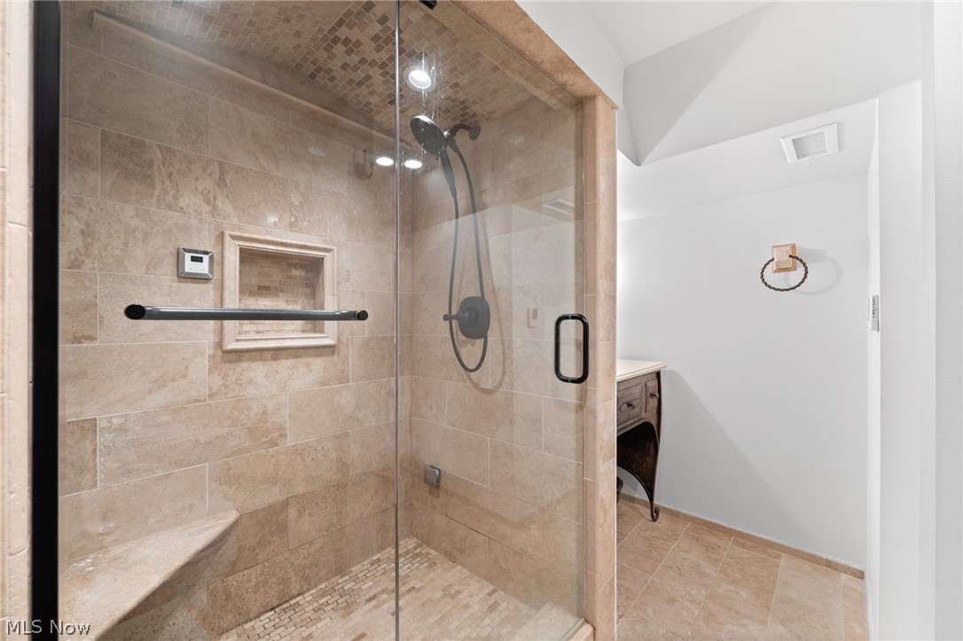 Walk-in shower with beige stone tile, mosaic floor, built-in niche, and corner bench.