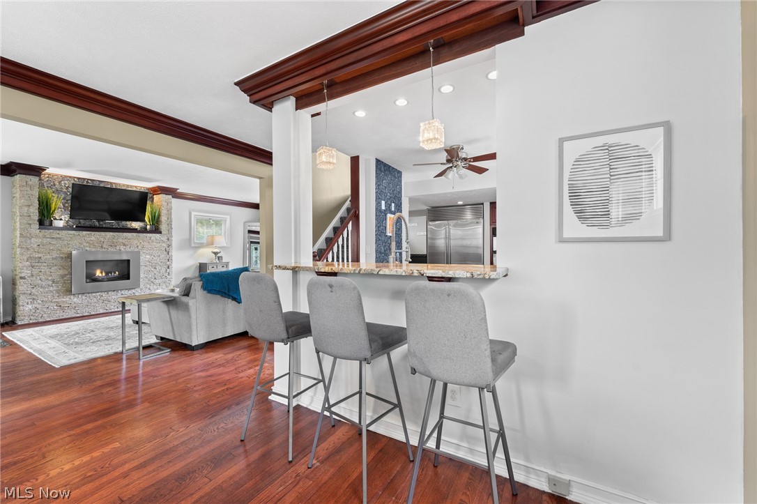 Open-plan kitchen and living room with a granite breakfast bar, stone fireplace, and hardwood floors.