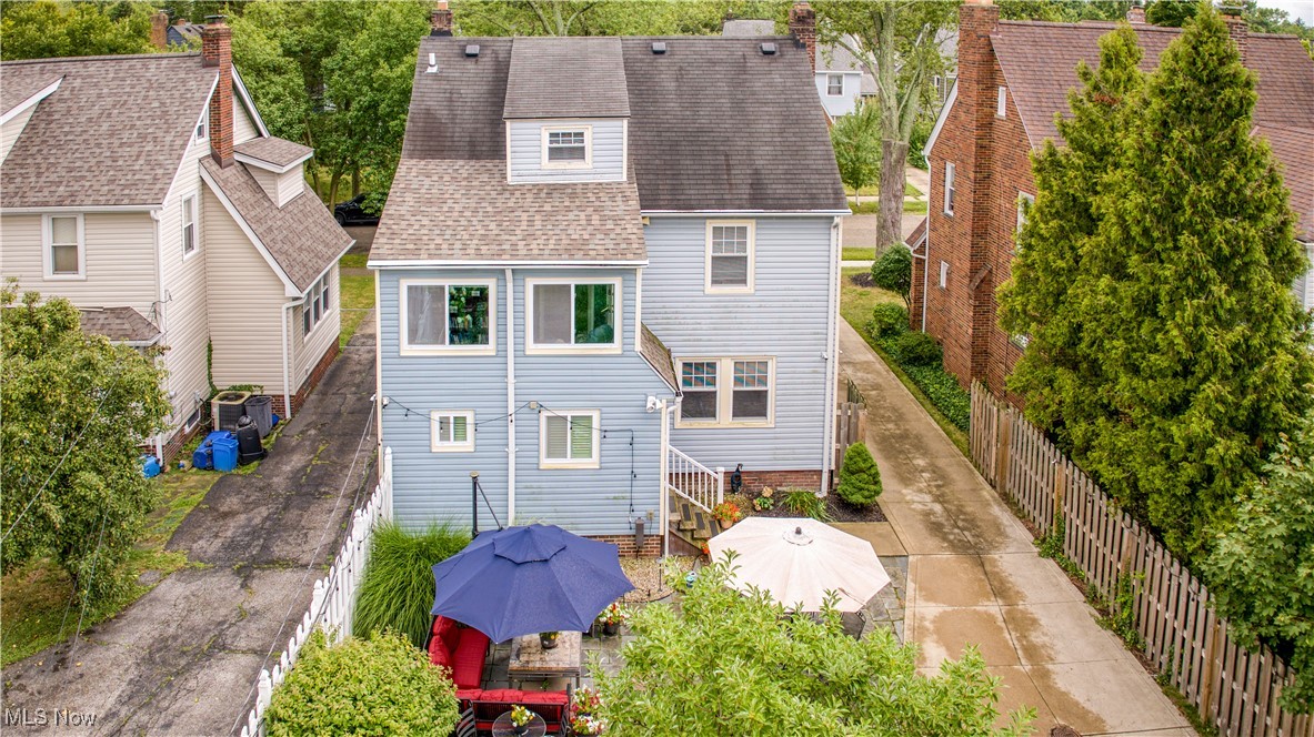 Rear of a blue-gray two-story house with a patio, umbrellas, and a paved side driveway.