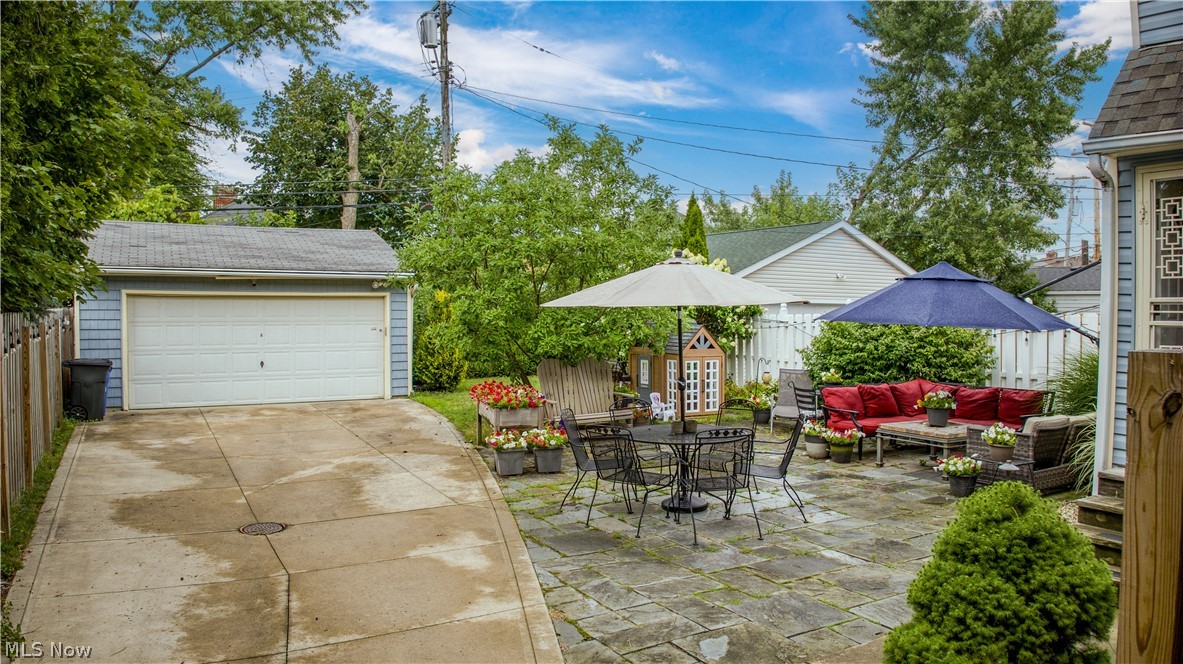 Backyard patio with umbrella-shaded seating, flower planters, driveway, and detached garage.