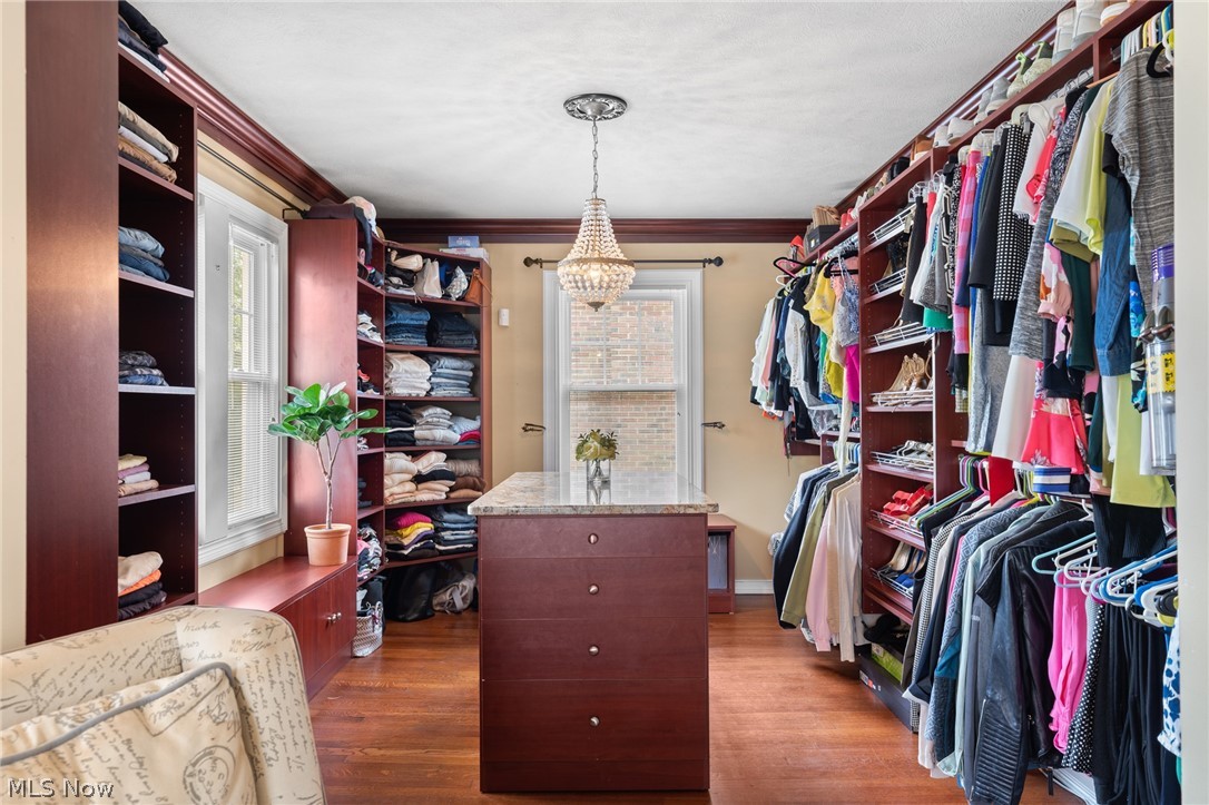 Walk-in closet with a central stone-topped island, dark wood built-ins, and a crystal chandelier.