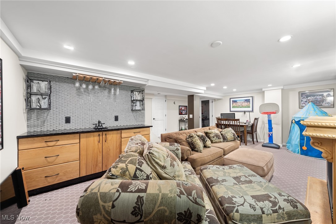 Basement recreation room with a sectional sofa, wet bar, dining table, and mini basketball hoop.