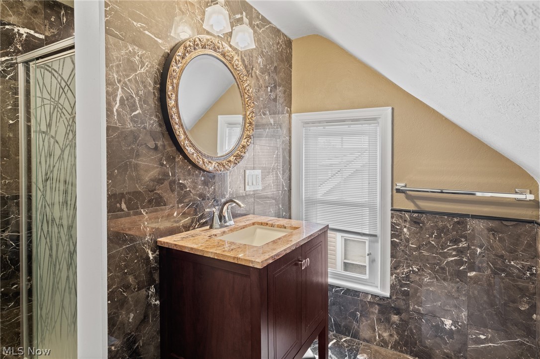 Bathroom with a dark wood vanity, stone countertop, ornate oval mirror, and marble-patterned tile.