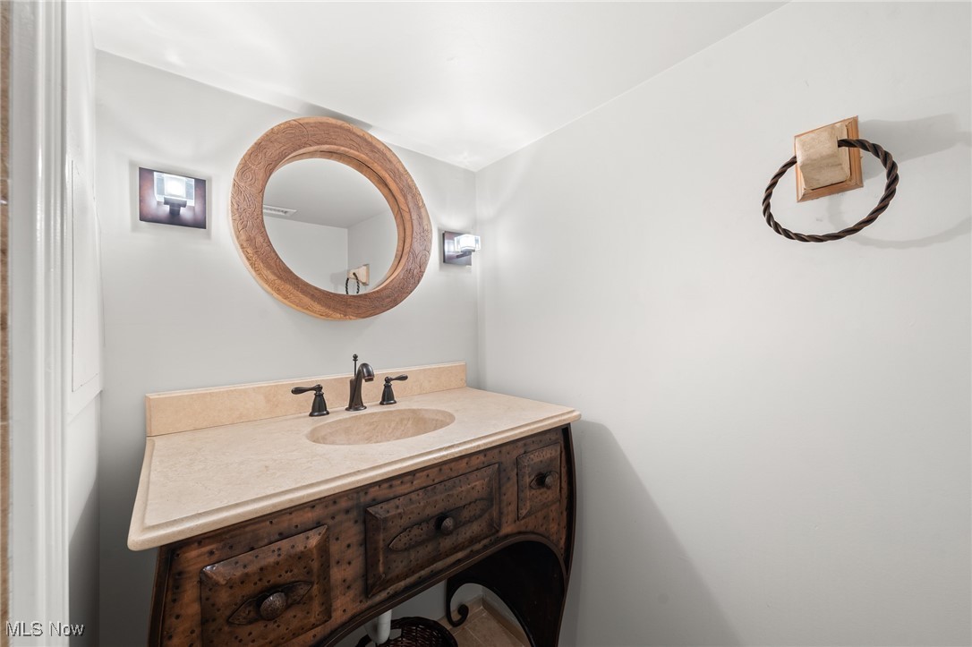 Bathroom vanity with a carved wood cabinet, stone sink, and large round framed mirror.