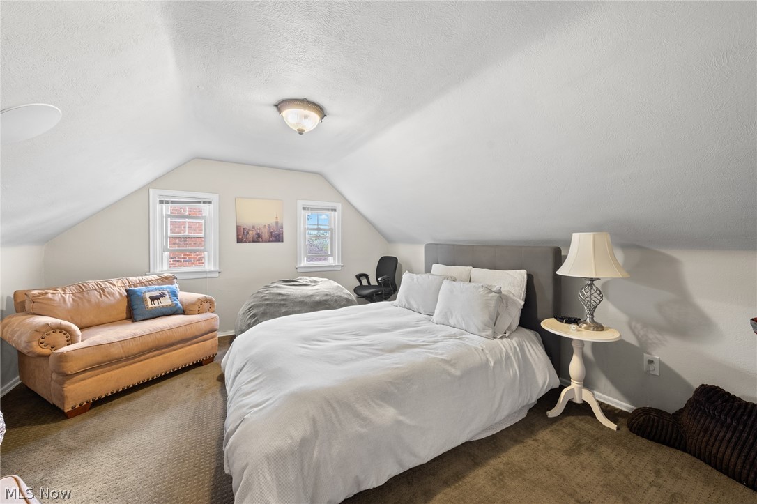 Bedroom with a white bed beneath a sloped ceiling and a tan leather loveseat.
