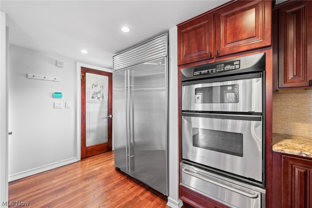 Kitchen with stainless steel refrigerator and double wall ovens, dark wood cabinets, and hardwood floors.