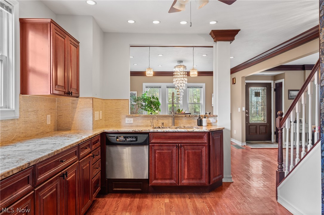 Kitchen with dark wood cabinets, stone counters, stainless steel dishwasher, and hardwood floors opening toward the foyer.