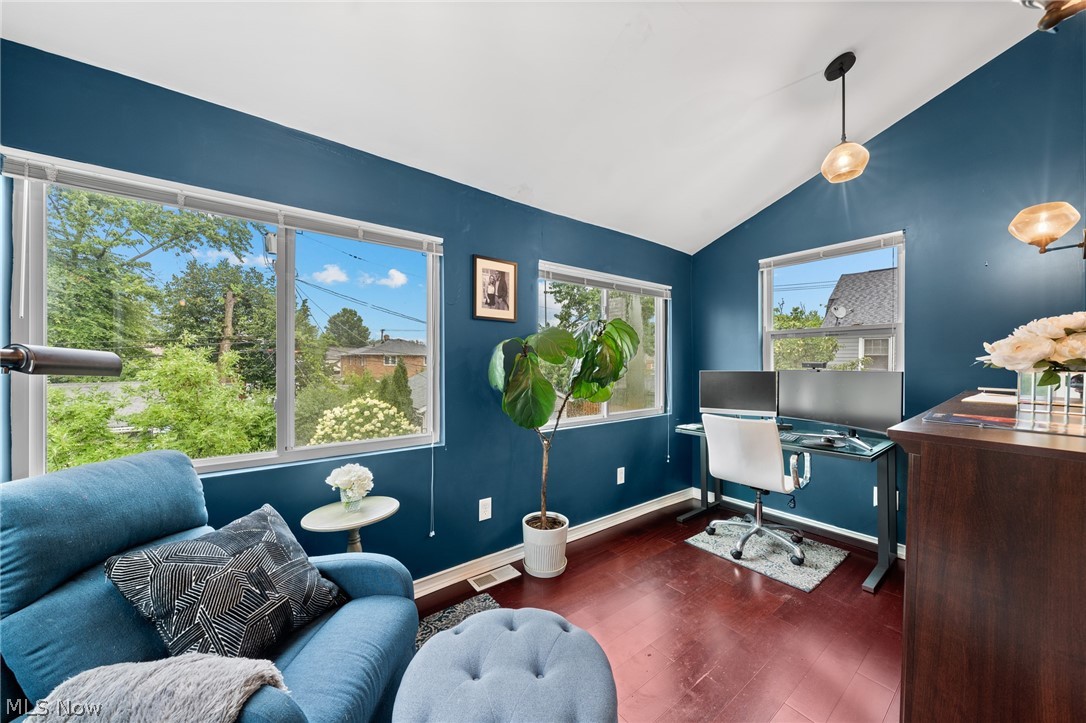 Home office with blue walls, a sofa, dual-monitor desk, and large windows overlooking trees.