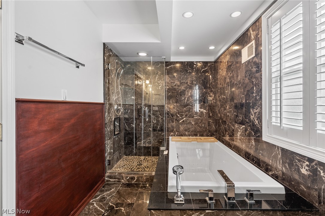 Bathroom with a white soaking tub, glass shower, and dark marble walls and floor.