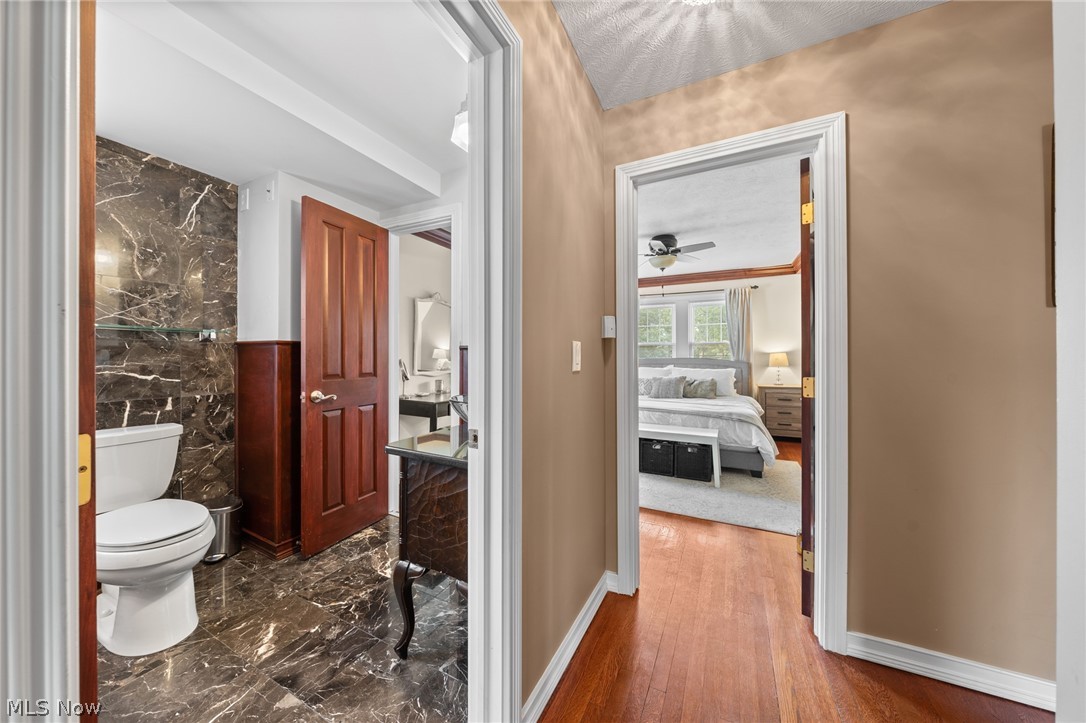 Hardwood hallway connecting a marble-floored bathroom and a bedroom with a light rug.
