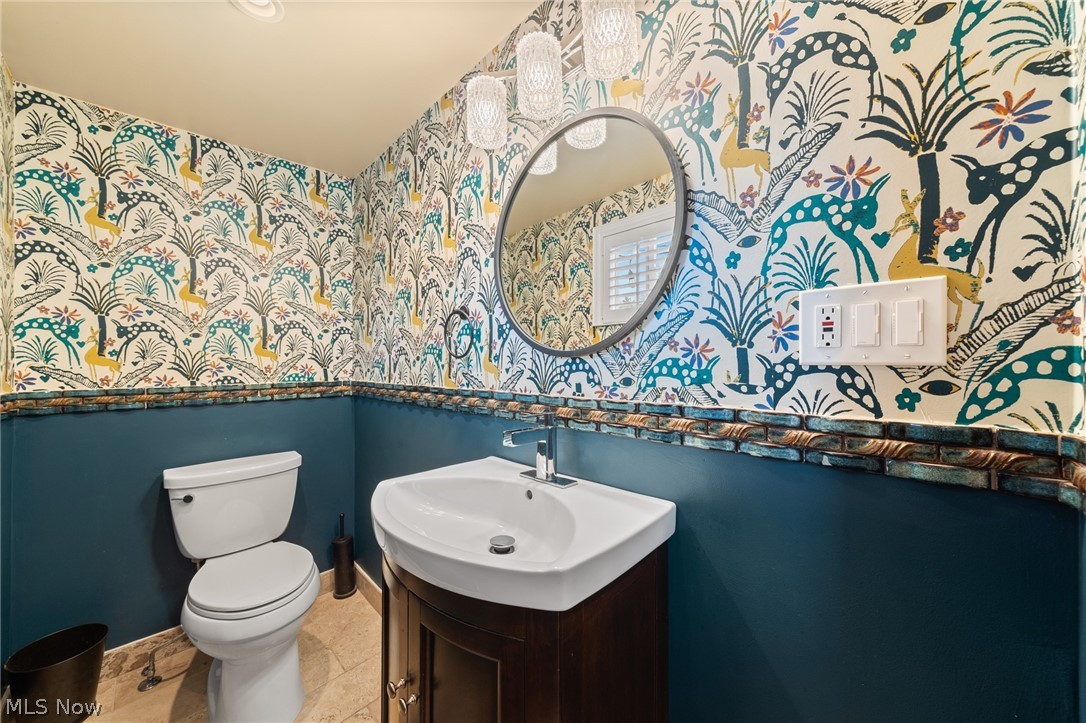 Bathroom with botanical wallpaper, teal lower walls, a round mirror, and a white sink and toilet.