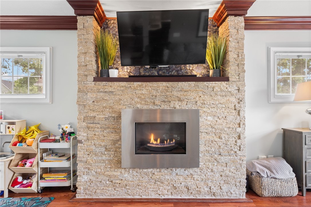 Living room fireplace with a large television, stone surround, and lit gas fire.