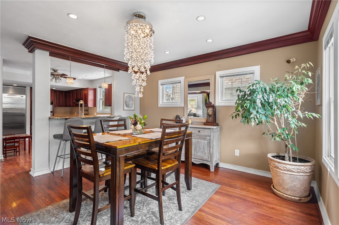 Dining room with a crystal chandelier, dark wood table, hardwood floors, and an open kitchen.