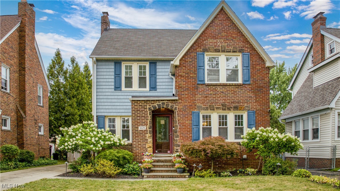 Two-story brick and blue-sided home with blue shutters and landscaped entry.