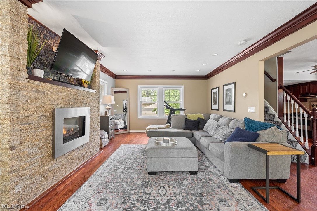 Living room with a stone fireplace, gray sectional, patterned rug, and hardwood floors.