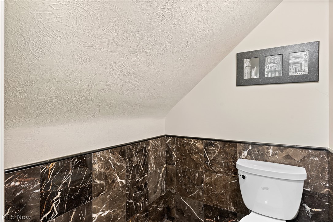 Bathroom with dark marble-pattern tile, a white toilet, and a sloped ceiling.
