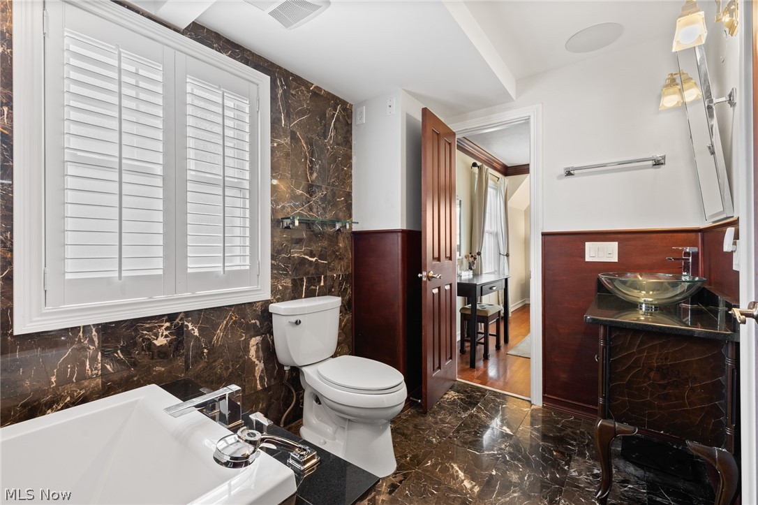 Bathroom with dark veined marble, a white bathtub, plantation shutters, and a glass vessel sink.