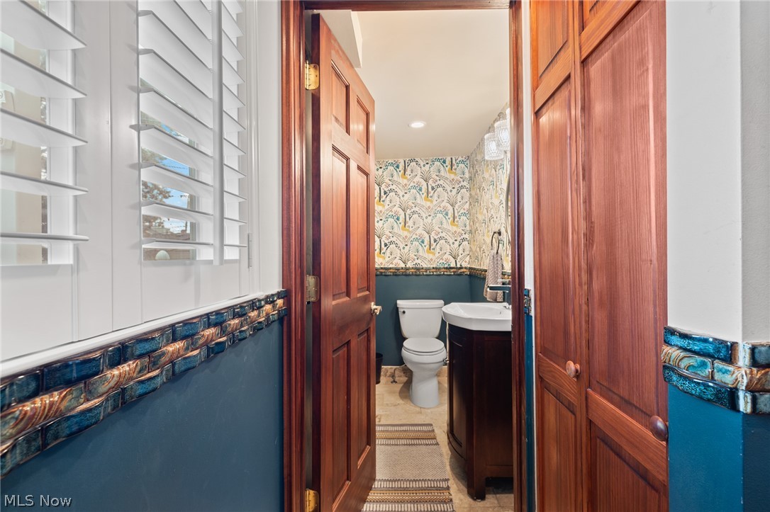 Bathroom with floral wallpaper, blue tile trim, plantation shutters, and a dark wood vanity.