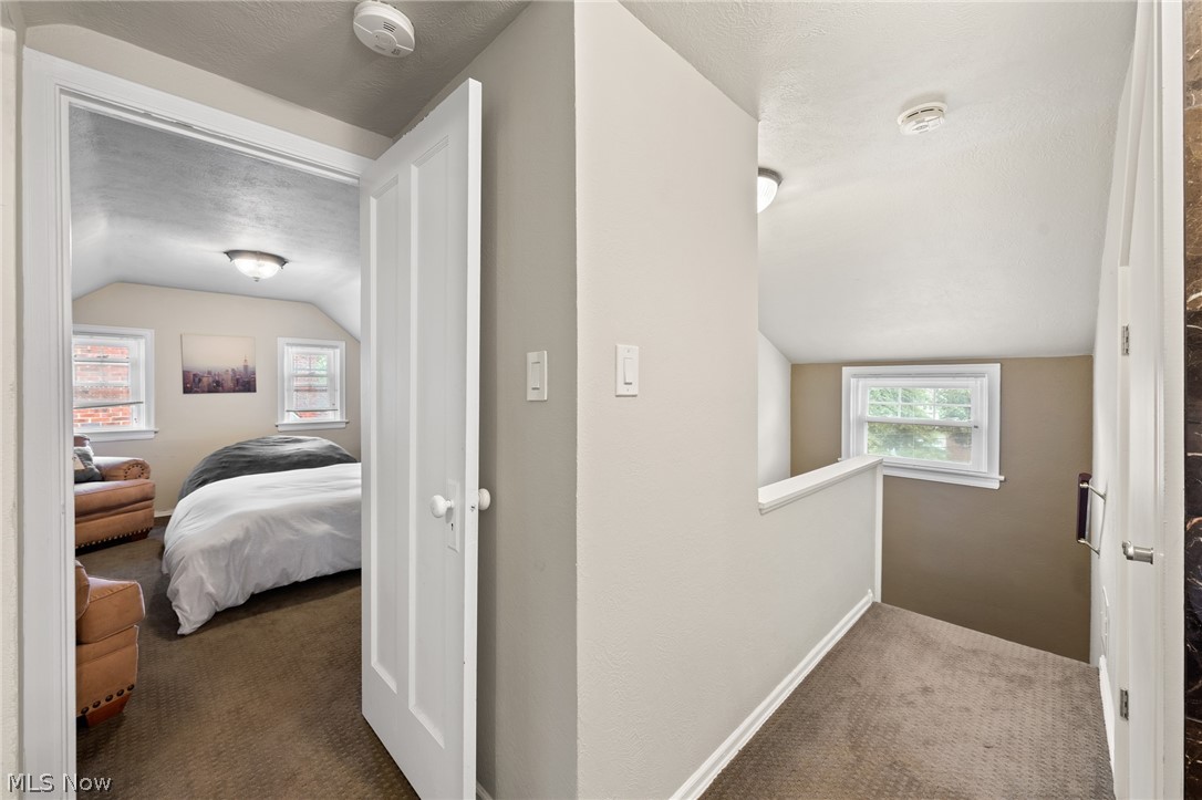 Upstairs hallway leading to a furnished bedroom with a bed and leather seating.