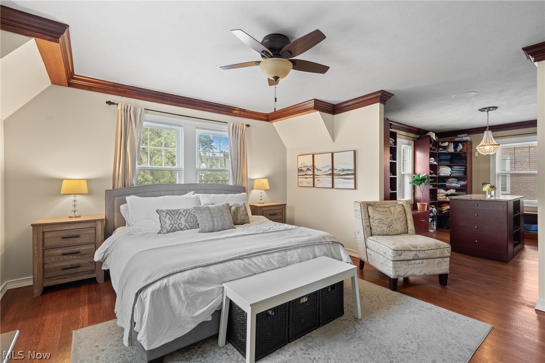 Furnished bedroom with a large bed, wood floors, ceiling fan, and open dressing area.