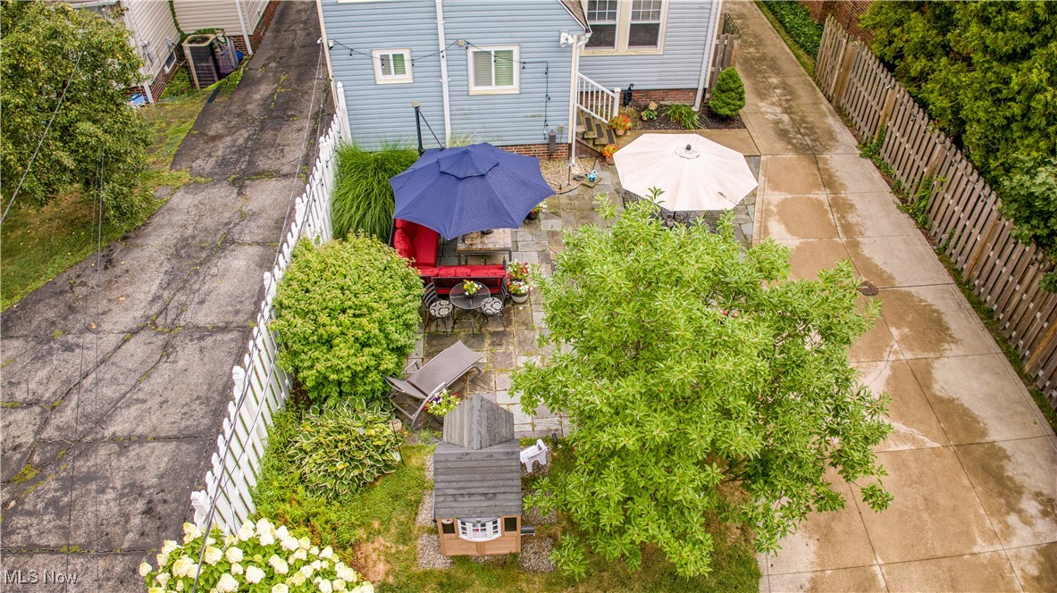 Aerial view of a landscaped backyard with a furnished stone patio, umbrellas, mature trees, and a playhouse.