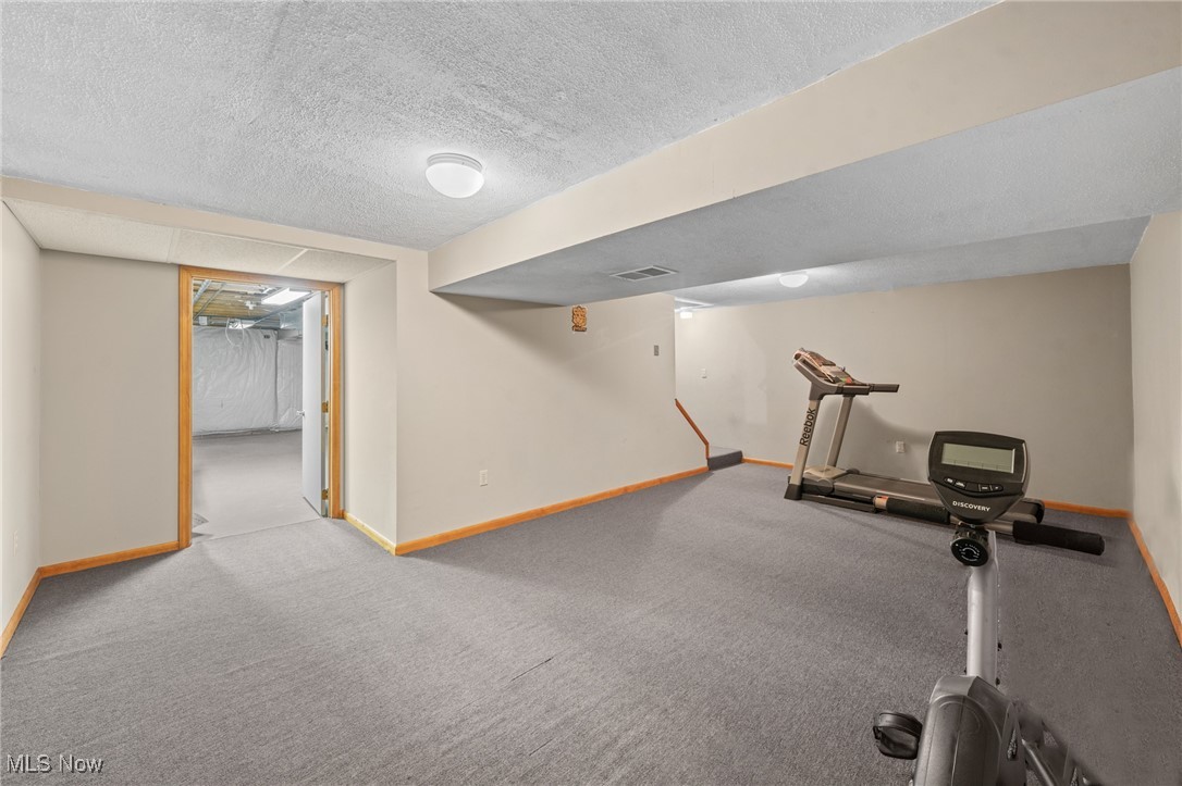 Basement exercise area with a treadmill, stationary bike, and doorway to an unfinished room.