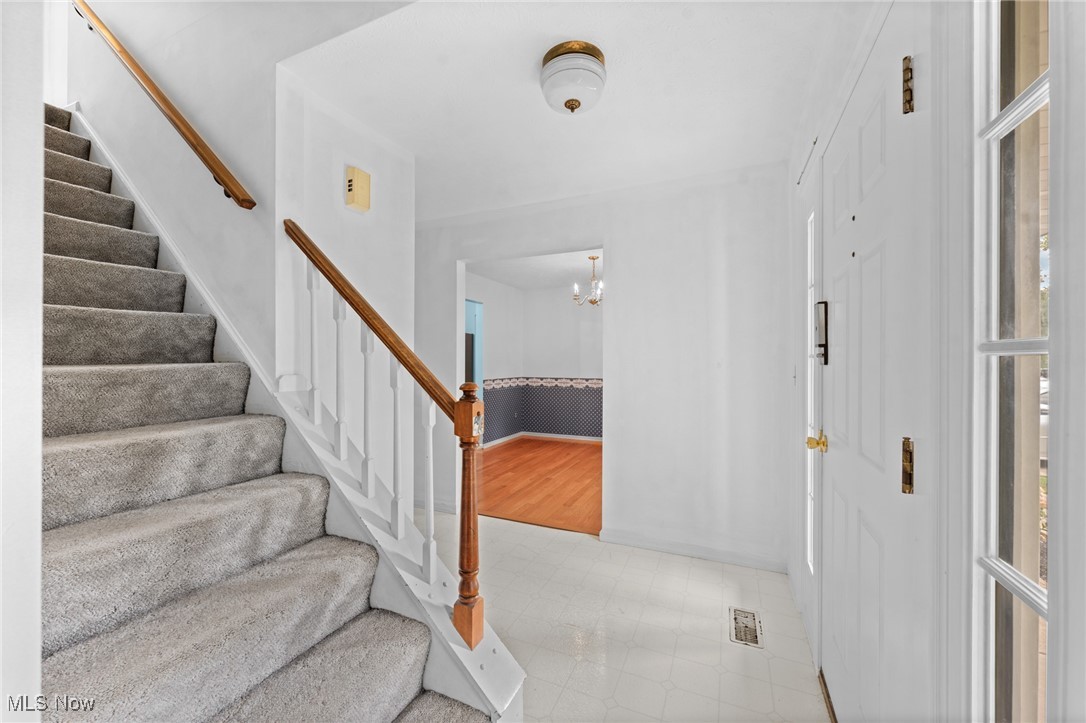 Entryway with a carpeted staircase, wood handrail, white tiled floor, and front door.