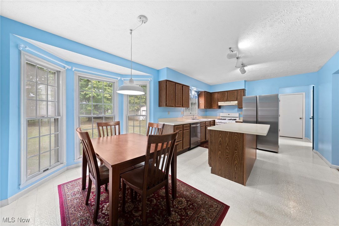 Kitchen and dining area with a central island, dark wood cabinets, and large bay windows.