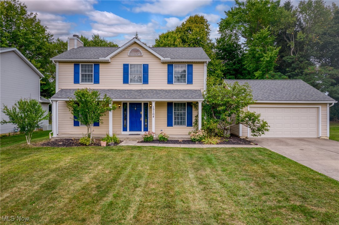 Two-story beige house with blue shutters and door, attached garage, landscaped beds, and a broad front lawn.