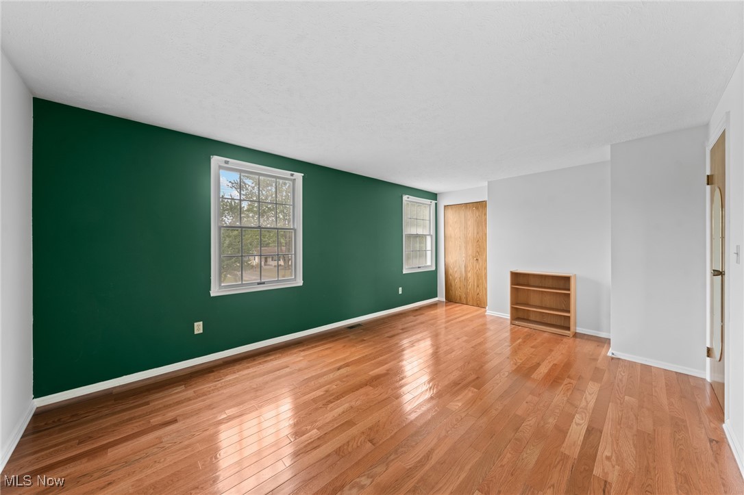 Empty bedroom with a green accent wall, hardwood floors, and two windows.