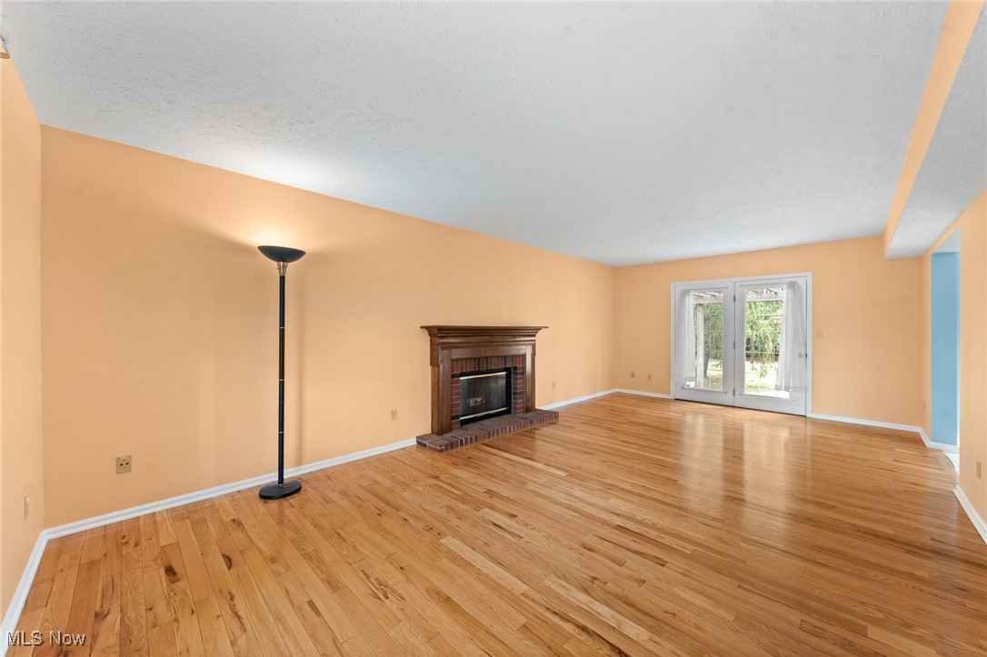Empty living room with hardwood floors, a brick fireplace, and glass double doors to the yard.