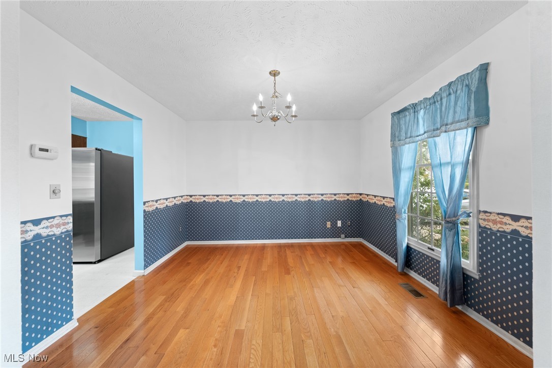 Empty dining room with hardwood floors, blue patterned walls, a chandelier, and tall curtained window.