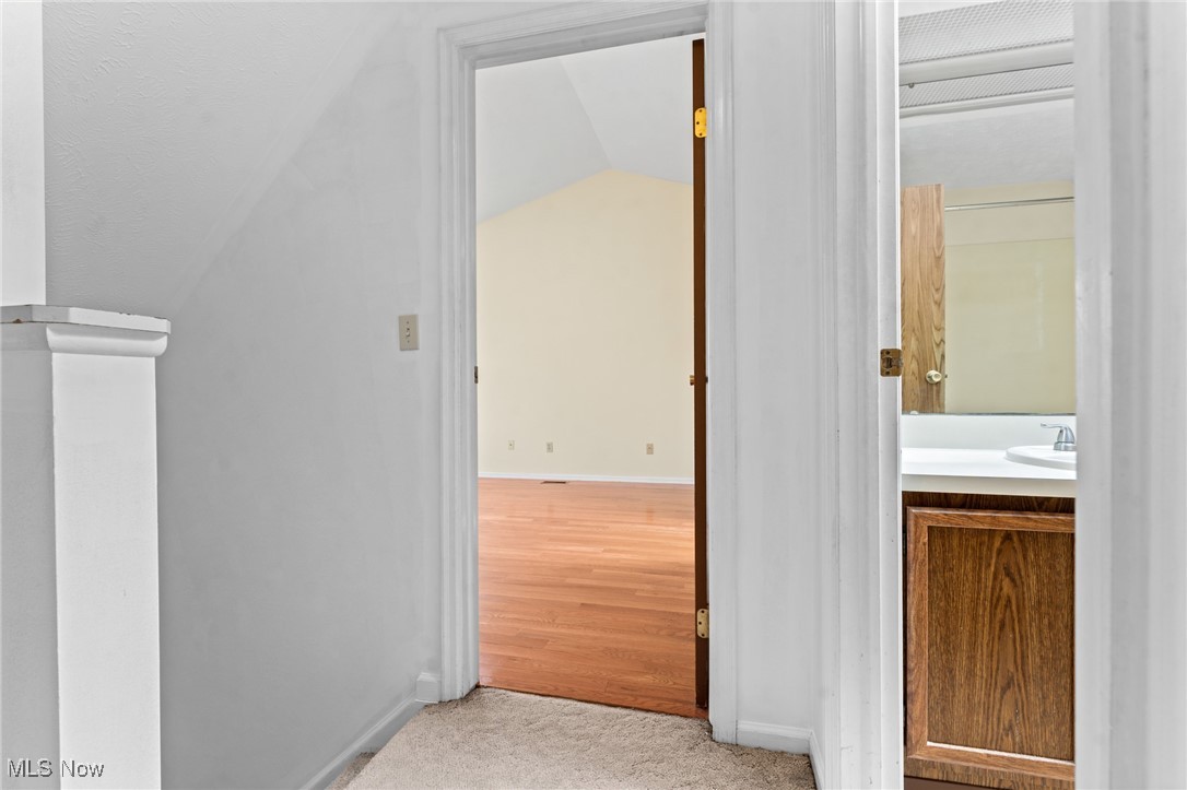 Carpeted hallway opens to an empty hardwood-floored room, with a bathroom vanity visible on the right.