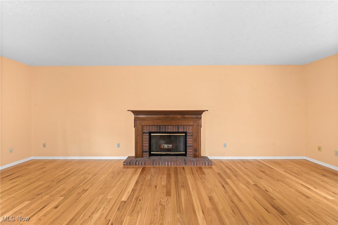 Vacant living room with hardwood floors and a brick fireplace beneath a dark wood mantel.