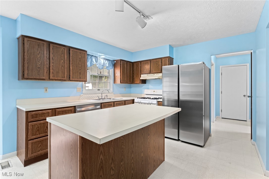 Kitchen with a large wood island, dark cabinets, and stainless steel refrigerator.