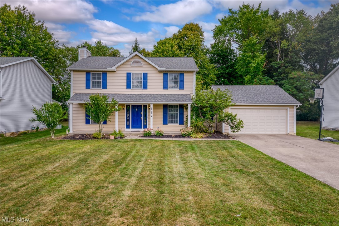 Two-story beige home with blue shutters, a blue front door, attached garage, and broad lawn.